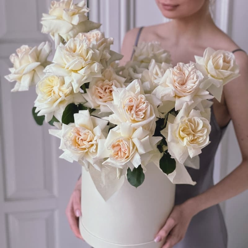 Person holding a large bouquet of white and beige roses in a box.