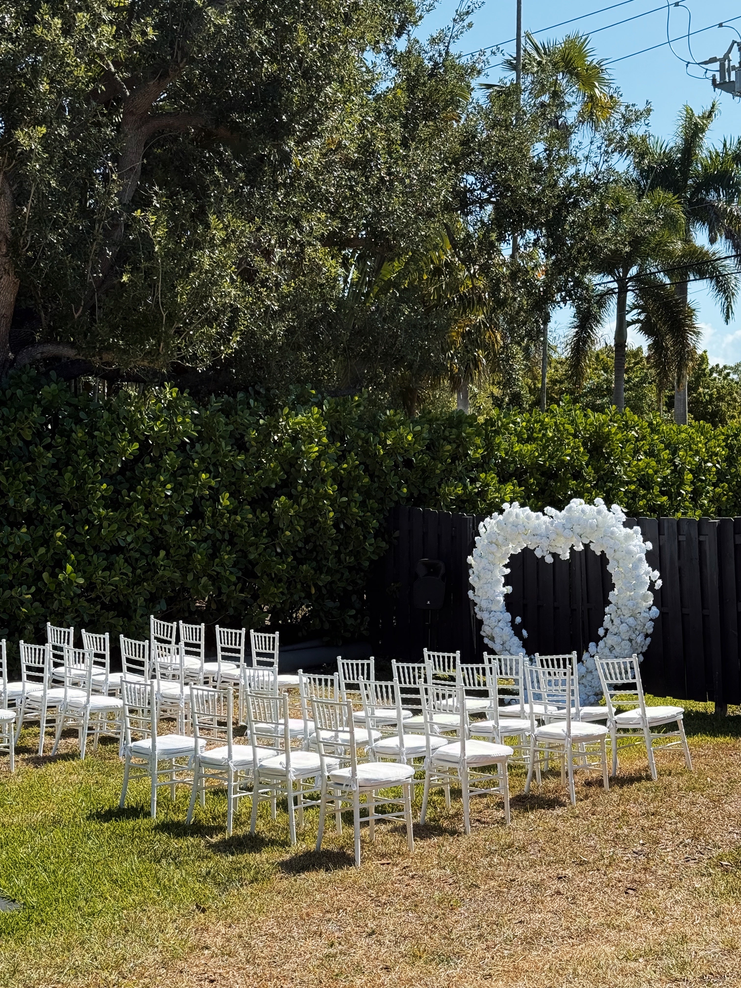 Outdoor wedding setup with white chairs and a heart-shaped floral arch.